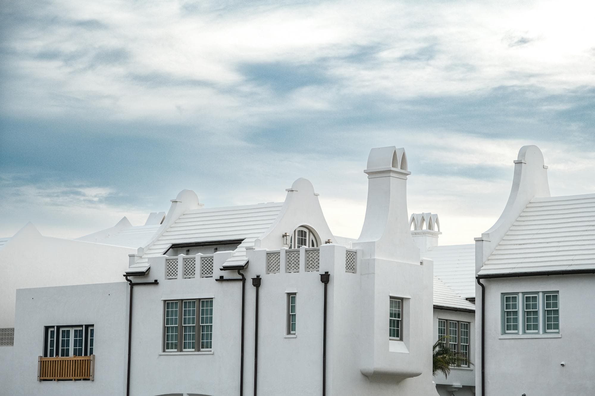 A cluster of white-stucco Alys Beach homes against a bright coastal sky — the kind of community we walk room by room.