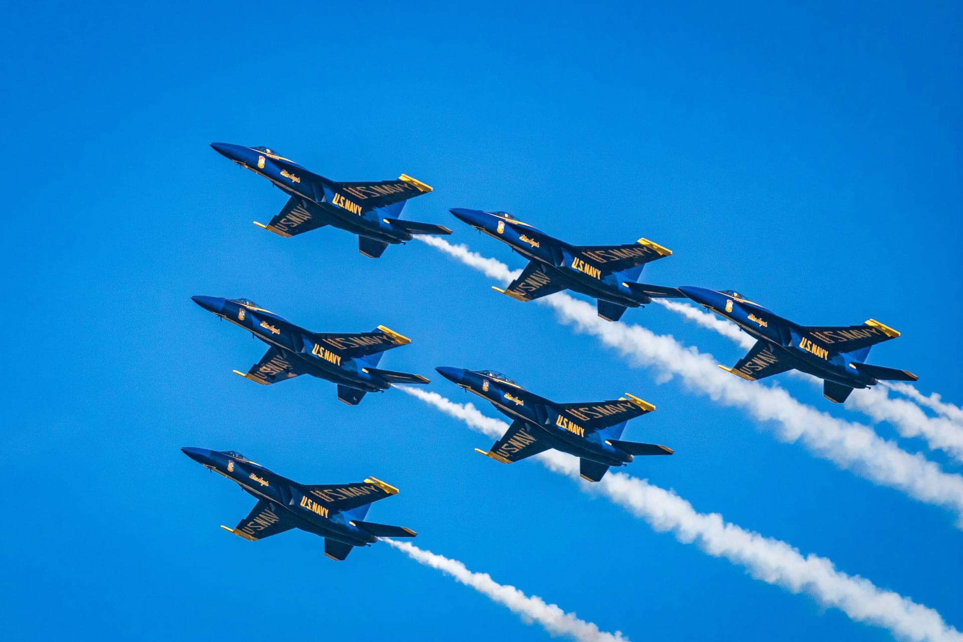 Six U.S. Navy Blue Angels F/A-18 jets flying in tight formation against a deep blue sky over Pensacola.