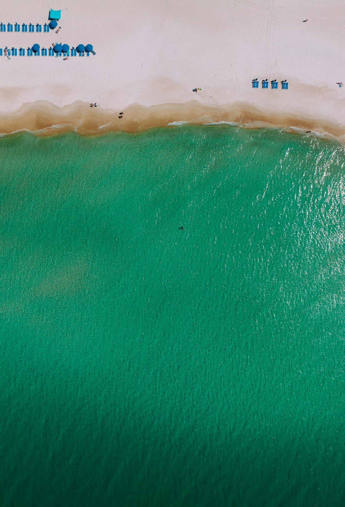 Aerial view of beach umbrellas lining the white sand beside emerald Gulf water along Miramar Beach, Florida.