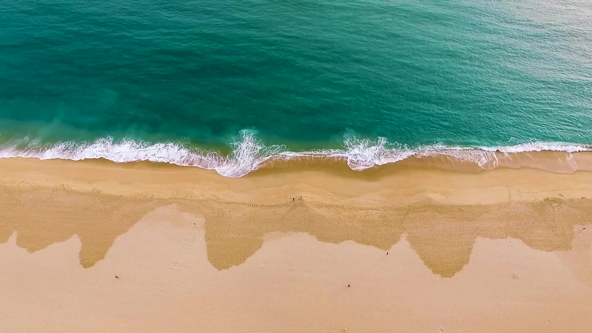 Aerial view over Florida's Emerald Coast — emerald Gulf water meeting a sweep of sugar-white sand, gentle waves breaking on the shoreline.